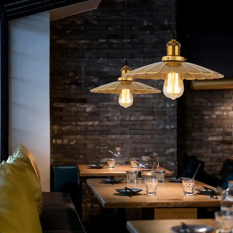 Gold wrought iron industrial pendant light with frosted glass shades hanging above wooden dining tables