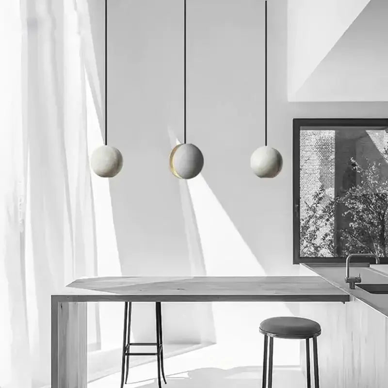 Three minimalist gray and gold decorbites cement pendant lights hang above a modern table as a dining room pendant light