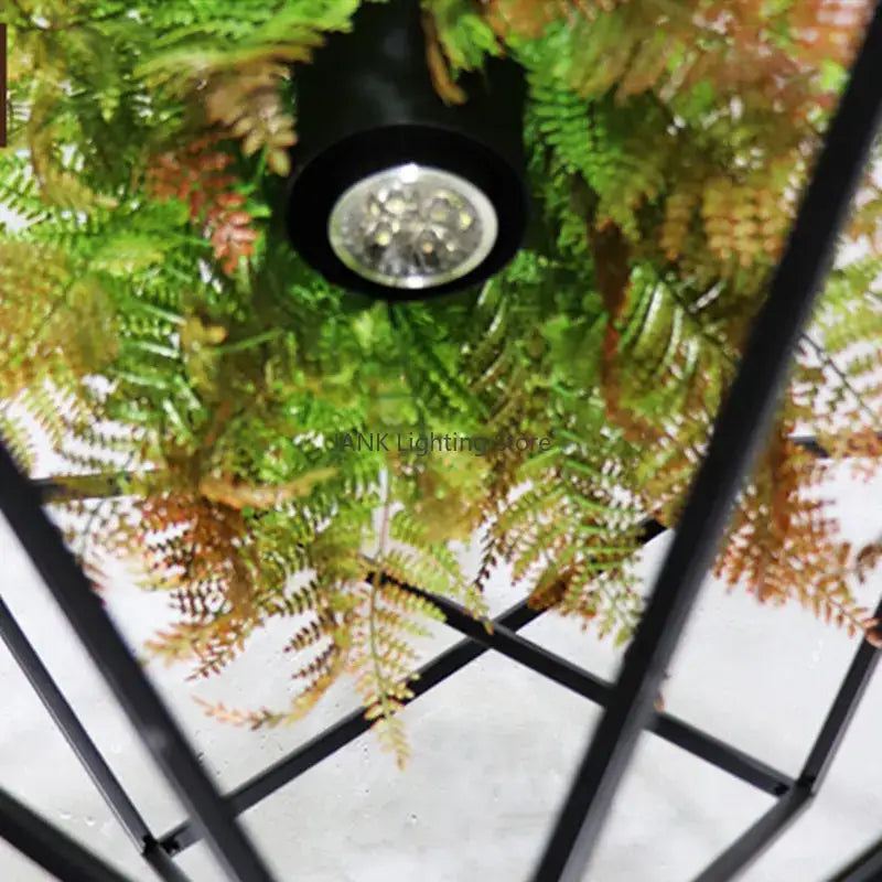 Black cylindrical led spotlight with clear lens mounted above green and brown ferns in decorbites industrial greenery chandelier