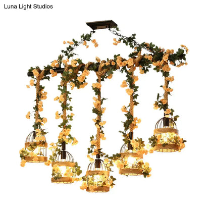 A rustic black decorbites™ birdcage chandelier with five lights wrapped in industrial hemp rope and adorned with yellow roses for restaurant island lighting
