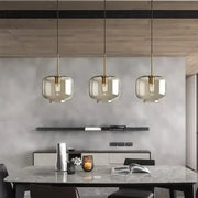 Three modern industrial glass pendant lights with smoked glass shades and brass accents hanging above dining table