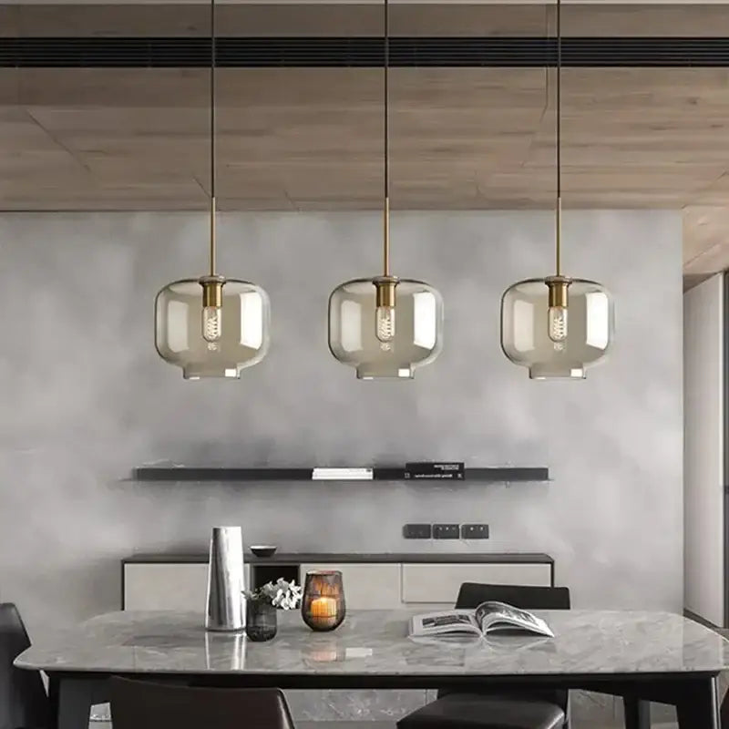 Three modern industrial glass pendant lights with smoked glass shades and brass accents hanging above dining table