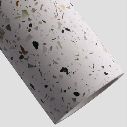 A cylindrical roll of white terrazzo material with black gray green and beige fragments for decorbites cement pendant lights