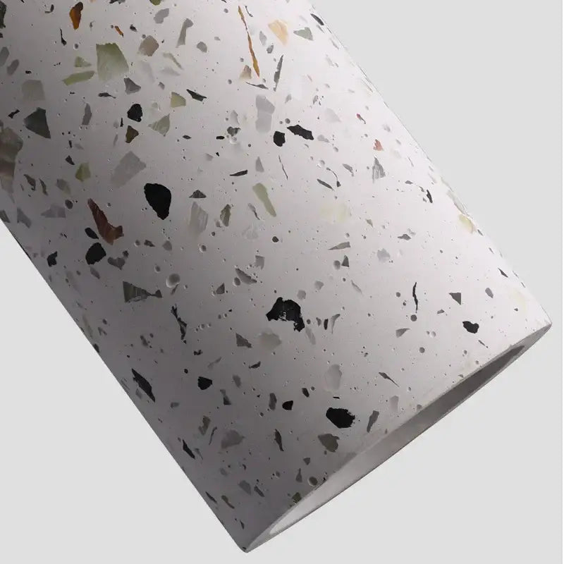 A cylindrical roll of white terrazzo material with black gray green and beige fragments for decorbites cement pendant lights