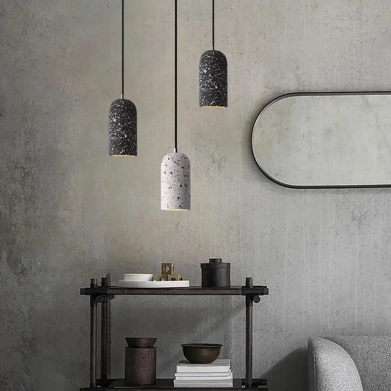 Three cylindrical industrial terrazzo cement pendant lights with speckled finishes hang against a gray wall for kitchen decor
