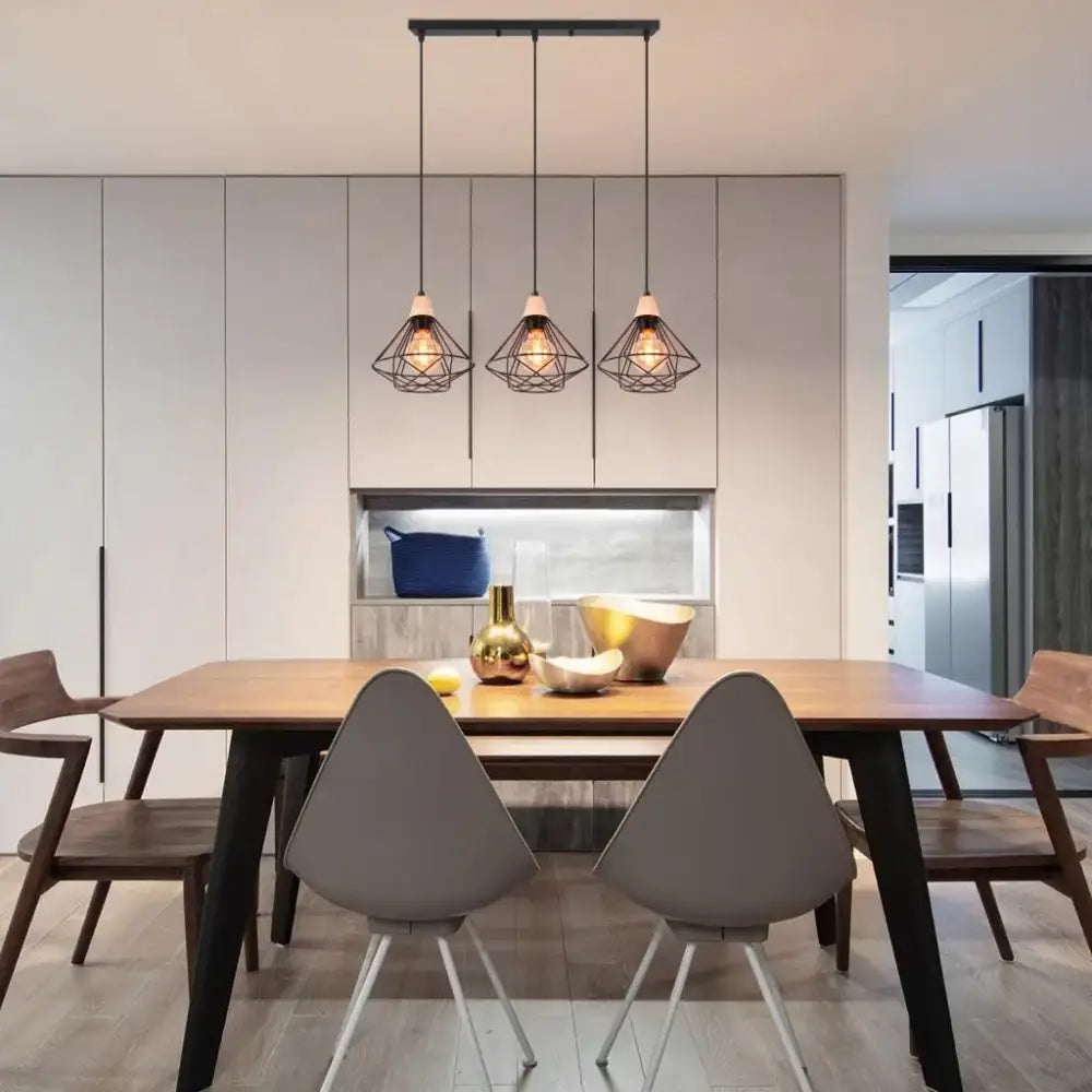 Three black metal cage pendant lights with warm bulbs hang above a wooden dining table in an industrial wood ceiling chandelier