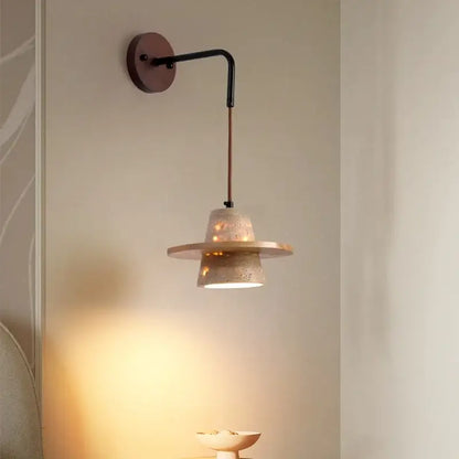 A modern wall lamp with a textured beige concrete shade, black metal arm, and pull chain switch for bedroom use