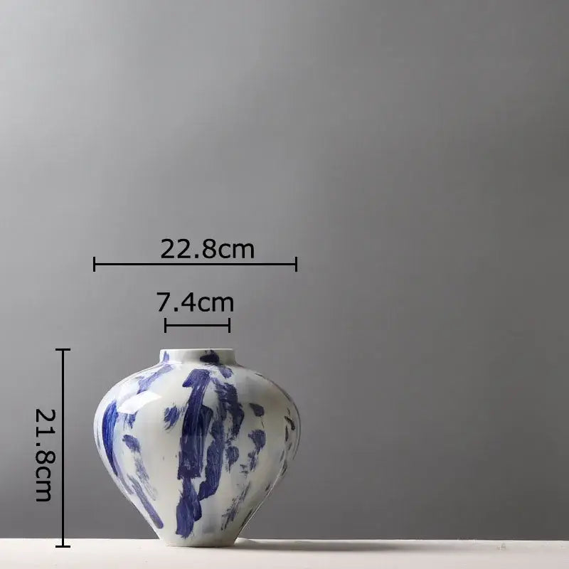 A white ceramic vase with bold blue ink style flowers and a rounded body with a narrow neck for living room decor