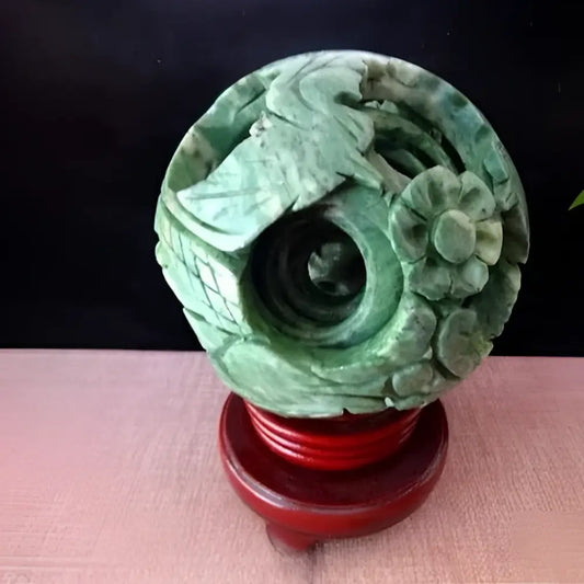 Intricate green jade stone dragon phoenix ball featuring carved bird and floral design on polished red wooden stand