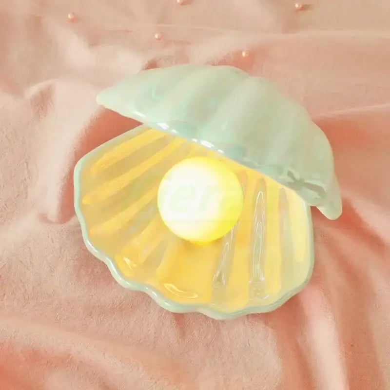 A delicate mint-green ceramic shell led night light with a glowing yellow orb for bedroom use