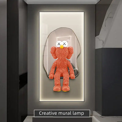 Orange kaws-style plush figure with white x-eyed face and yellow nose in sleek mirrored frame led wall lamp decor