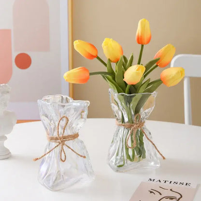Irregular folded clear glass vase by decorbites with textured surface and rustic twine holding yellow and orange tulips