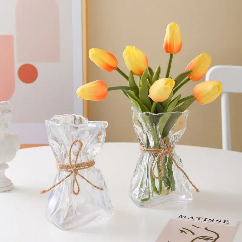 Irregular folded clear glass vase by decorbites with textured surface and rustic twine holding yellow and orange tulips