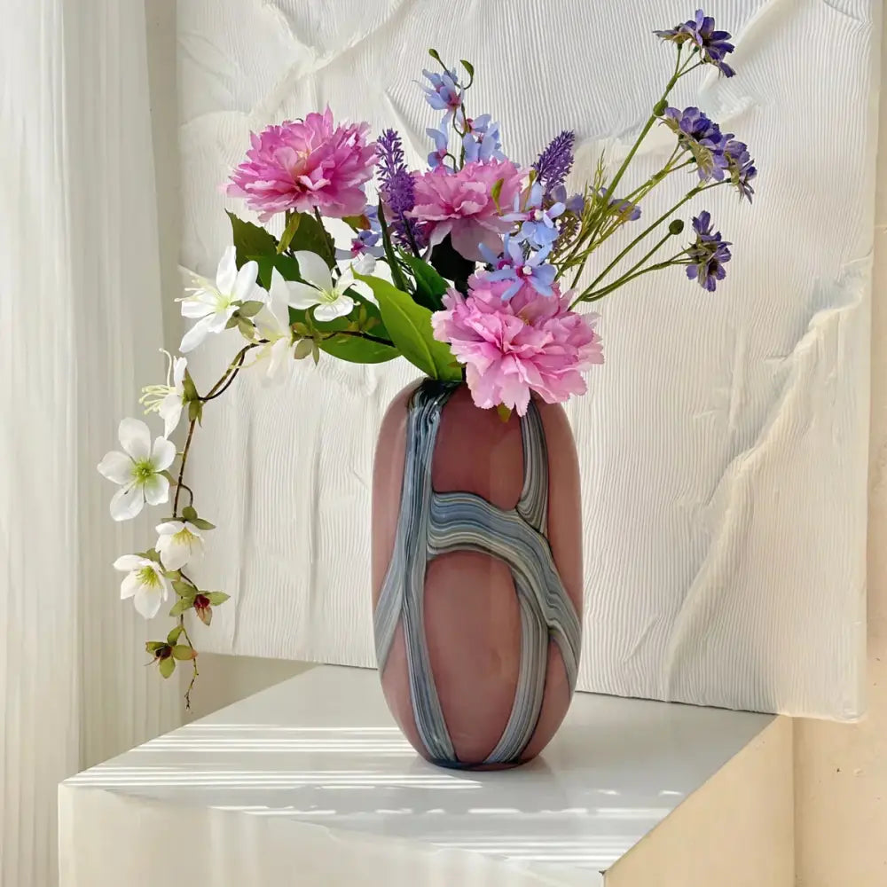 A blush pink glass vase with irregular geometric graffiti swirl patterns holds a vibrant floral bouquet for decorbites decor