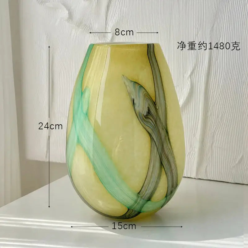 A glossy teardrop-shaped glass vase with irregular geometric green and dark gray marbled patterns on a pale yellow base decorbites irregular geometric decor