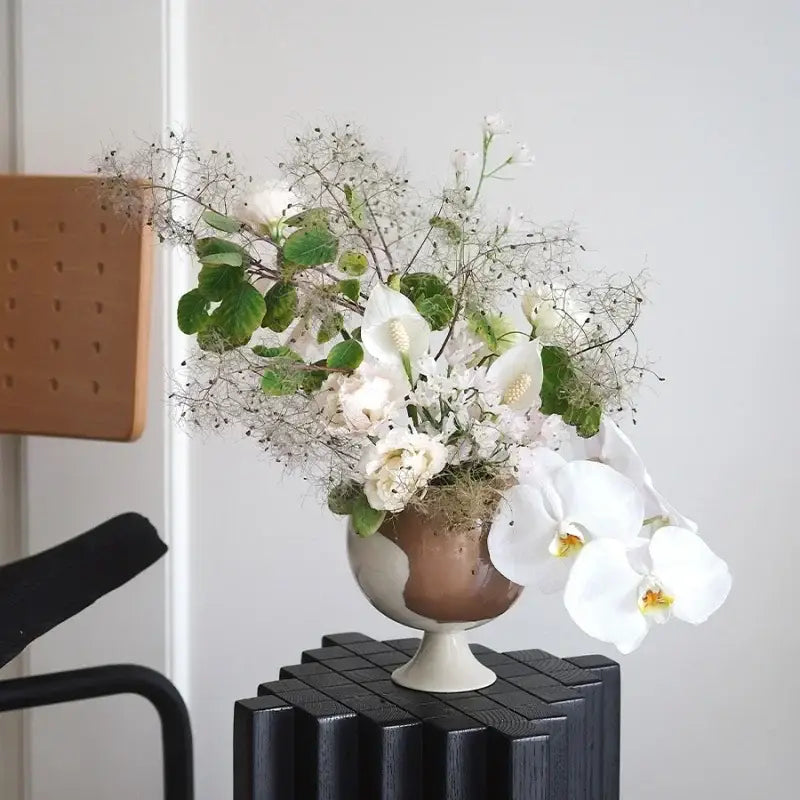 A ceramic irregular grain spherical vase in matte white and earthy brown holding white orchids and roses decorbites irregular grain