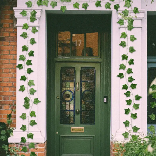 Ivy green fake leaves garland vine decorating a deep green wooden front door with stained glass panels and brass hardware