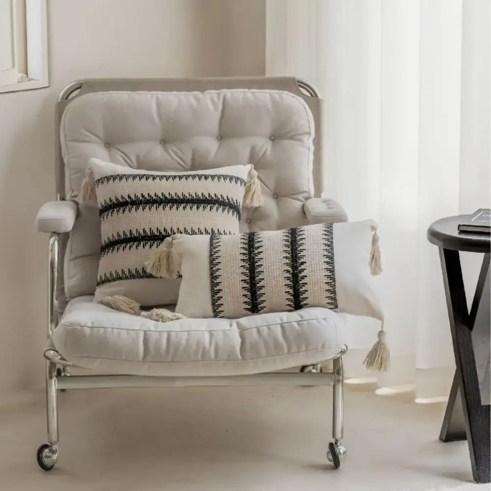 Beige tufted armchair with chrome frame and caster wheels featuring black and white decorbites jacquard crochet pillow covers