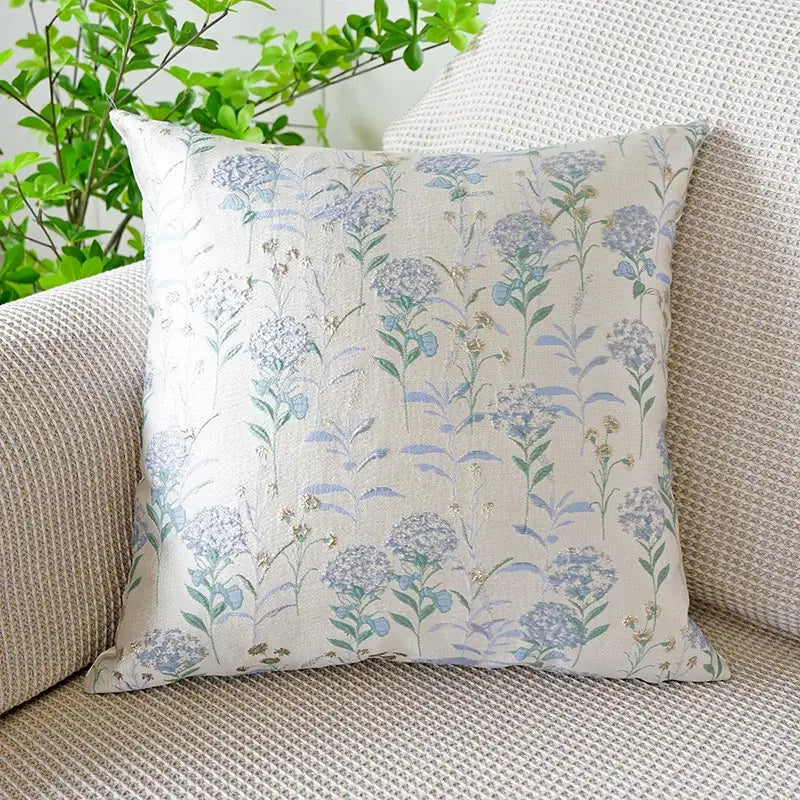 A jacquard floral pillow cover with delicate blue and green floral pattern and subtle metallic accents on off-white fabric