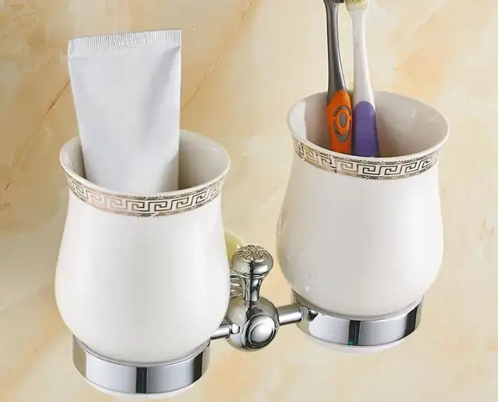 White ceramic toothbrush holder with silver Greek key trim and chrome base holding two brushes in jade bathroom set
