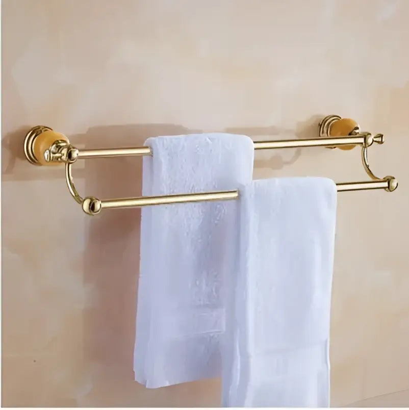 Gold-colored double towel rack with ornate ends and white towels from jade gold bathroom accessories set with amber marble