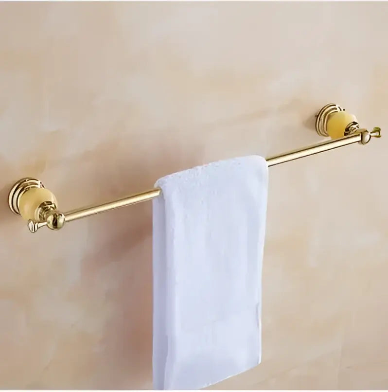 Gold-colored towel rack with ornate rounded ends and white towel in jade gold bathroom accessories set with amber marble