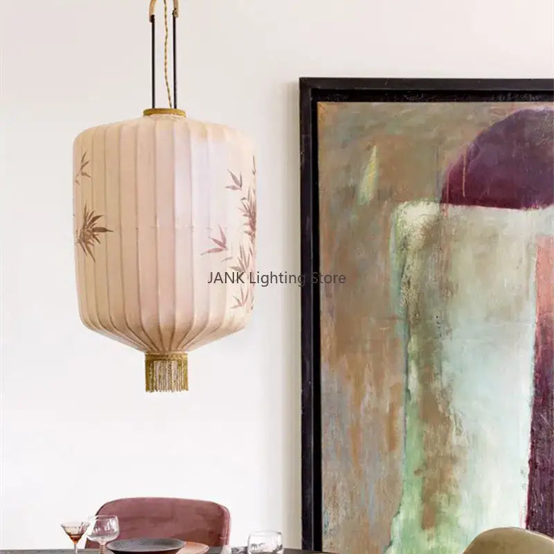 Beige pleated paper lantern with bamboo leaf pattern embroidery and gold fringe hanging as living room pendant light