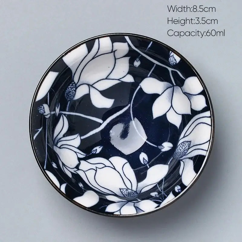 A small round decorbites ceramic kung fu tea bowl with glossy black glaze and delicate white floral patterns