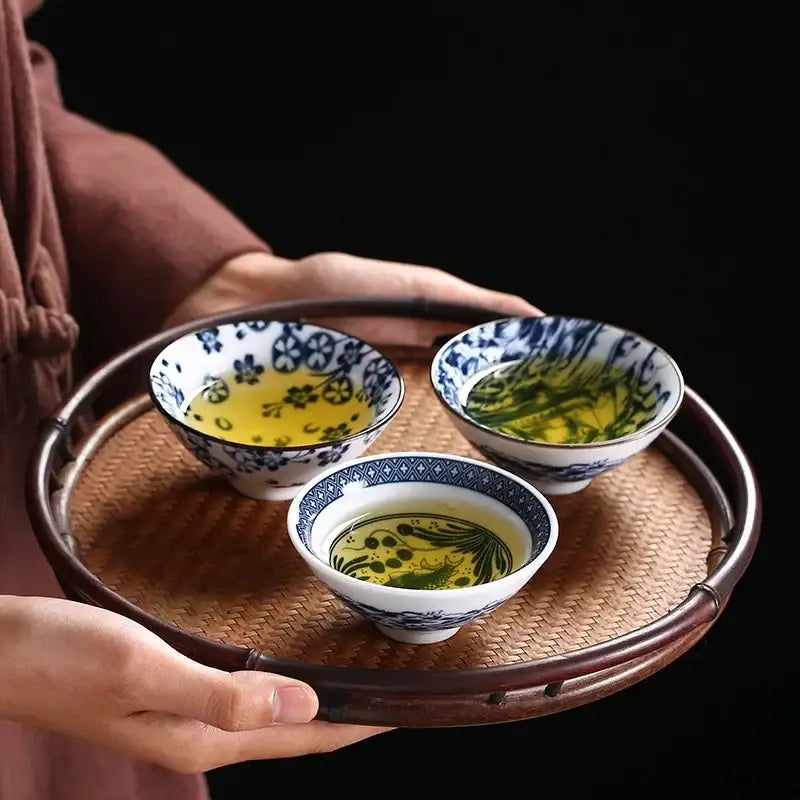 Three hand-painted decorbites ceramic kung fu tea bowls with blue floral patterns filled with greenish-yellow tea