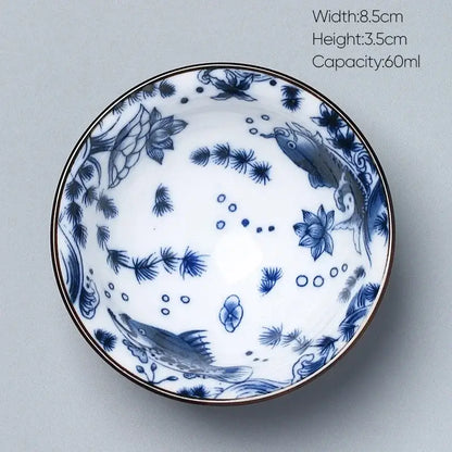 A delicate white porcelain kung fu tea cup with intricate blue fish and lotus designs and a thin gold rim by decorbites ceramic