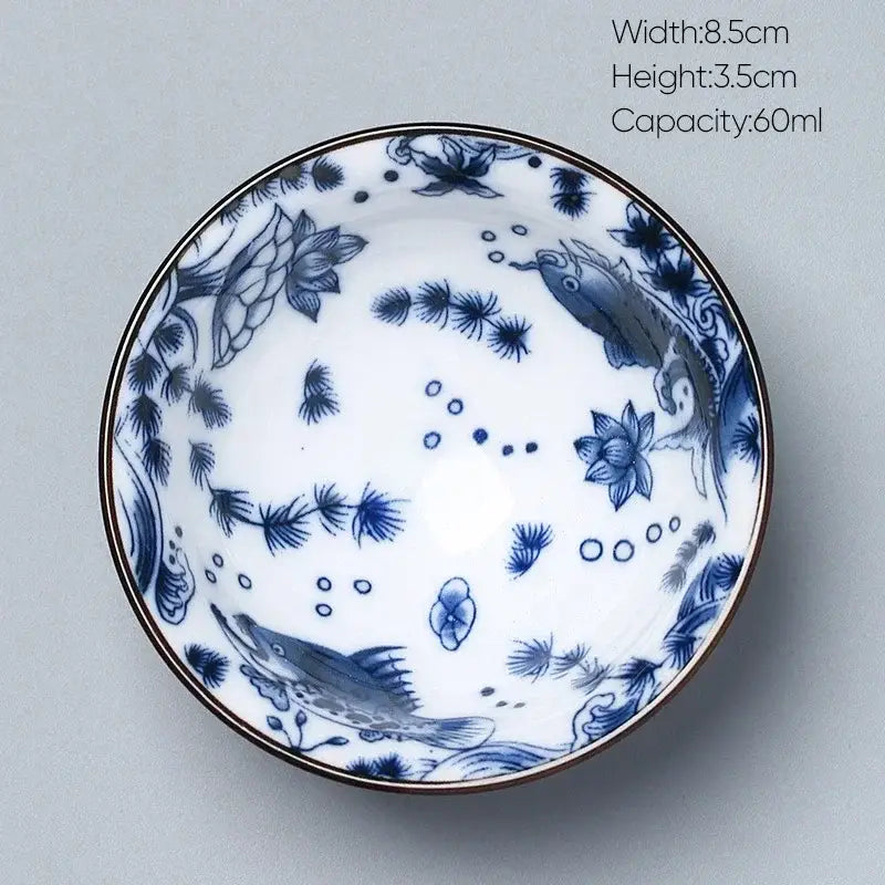 A delicate white porcelain kung fu tea cup with intricate blue fish and lotus designs and a thin gold rim by decorbites ceramic