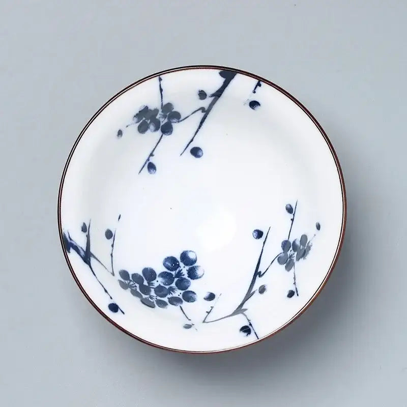 A white decorbites ceramic kung fu tea bowl with blue plum blossom patterns and a thin brown rim for dining room use