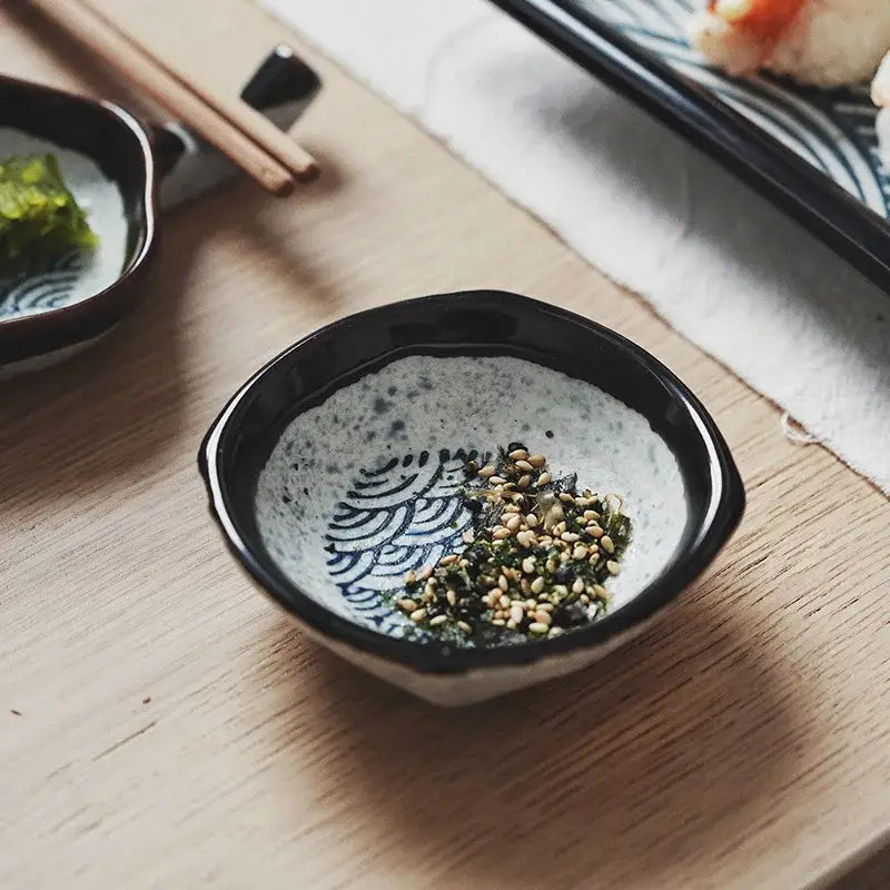 Black-rimmed ceramic japanese porcelain bowl with speckled interior and blue wave patterns holding sesame seeds and seaweed