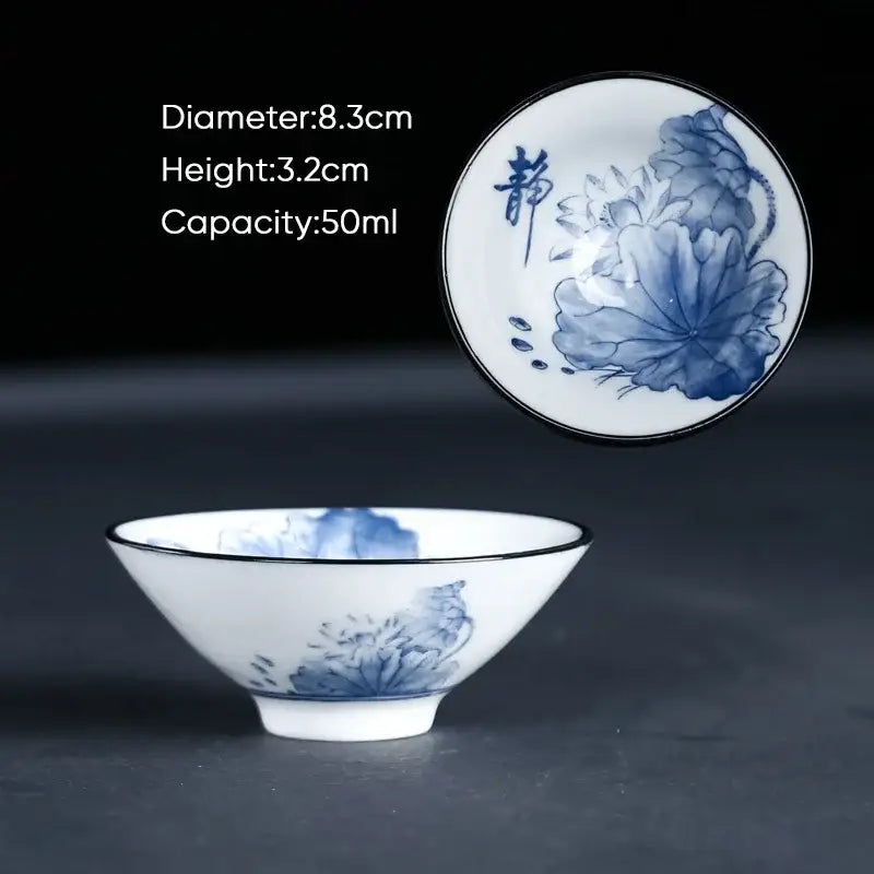 A delicate white porcelain ceramic kung fu tea cup with blue hand-painted lotus calligraphy and a black rim