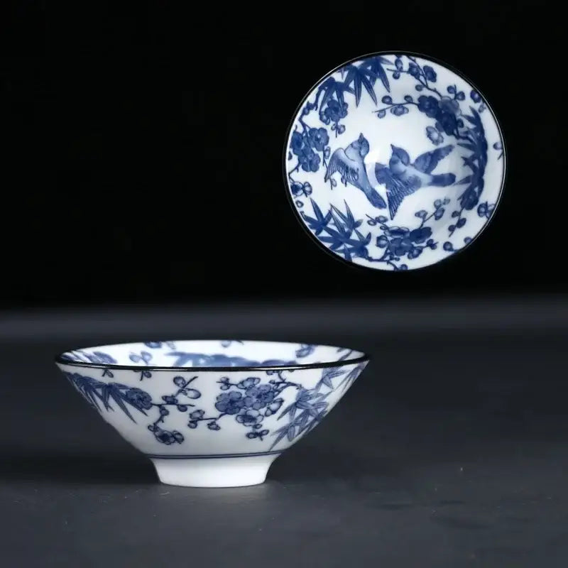 A delicate white porcelain ceramic kung fu tea cup with blue floral and bird motifs and a subtle black rim