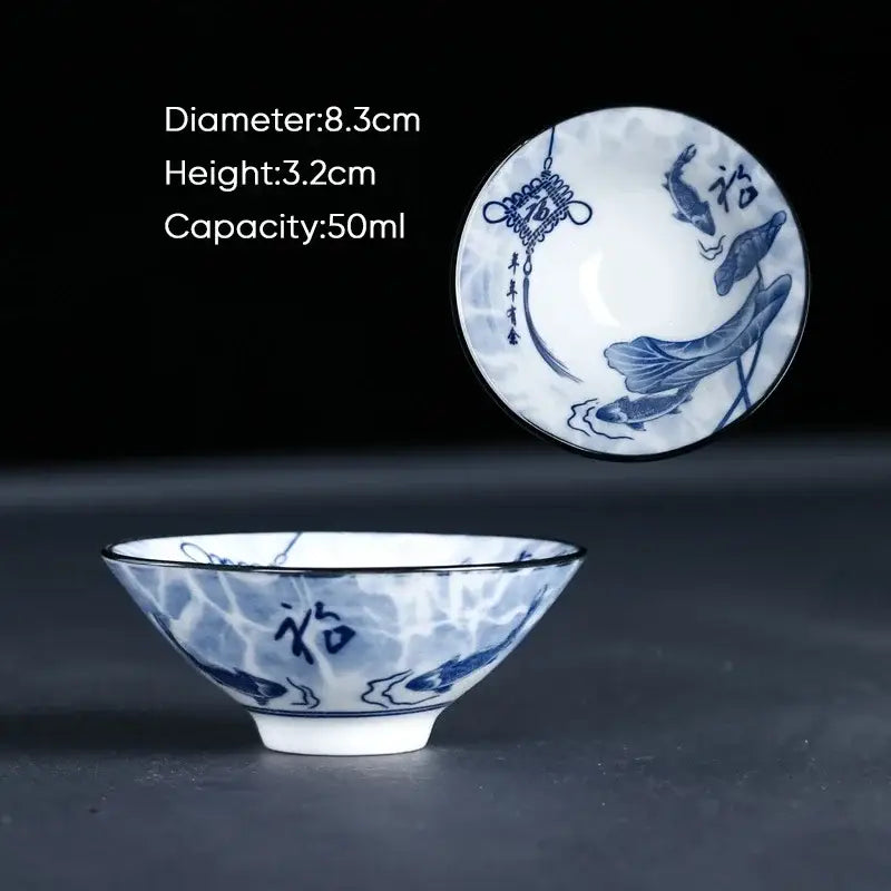 A delicate white porcelain ceramic kung fu tea cup with blue hand-painted fish and lotus auspicious motifs