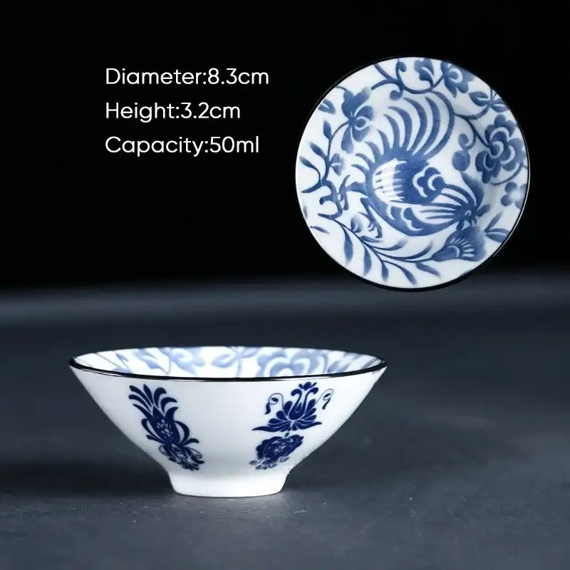 A delicate white porcelain ceramic kung fu tea cup with intricate blue floral and bird motifs and a thin black rim