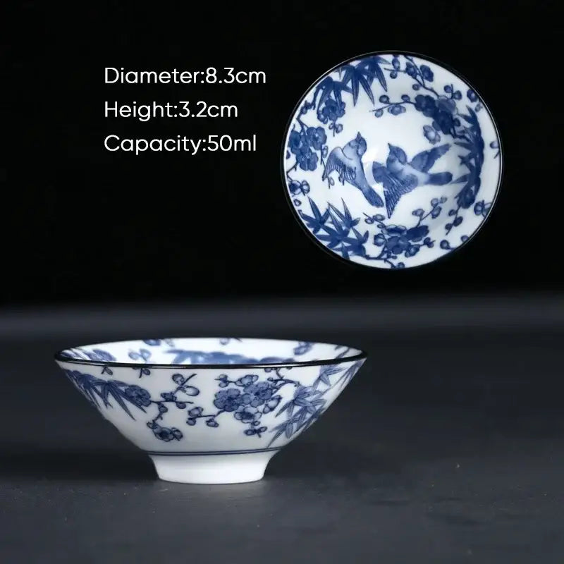 A delicate white ceramic kung fu tea cup with blue floral and bird motifs and a subtle black rim, perfect for tea