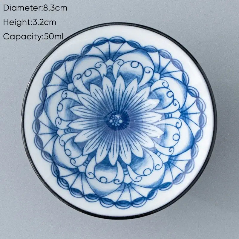 A delicate blue and white ceramic kung fu tea cup with an intricate floral mandala design and a black rim
