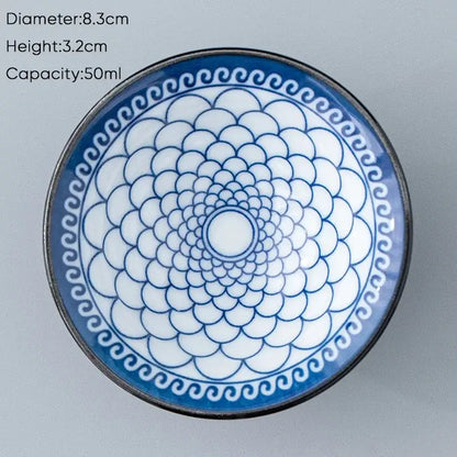 A white ceramic kung fu tea cup with blue scalloped pattern and black rim featuring intricate circular designs