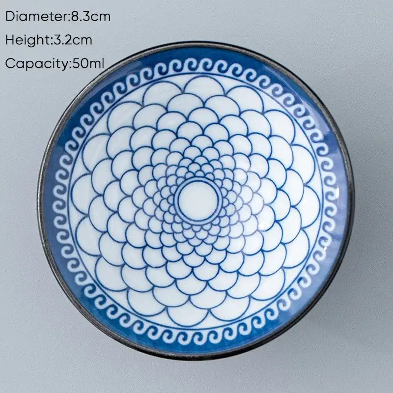 A white ceramic kung fu tea cup with blue scalloped pattern and black rim featuring intricate circular designs