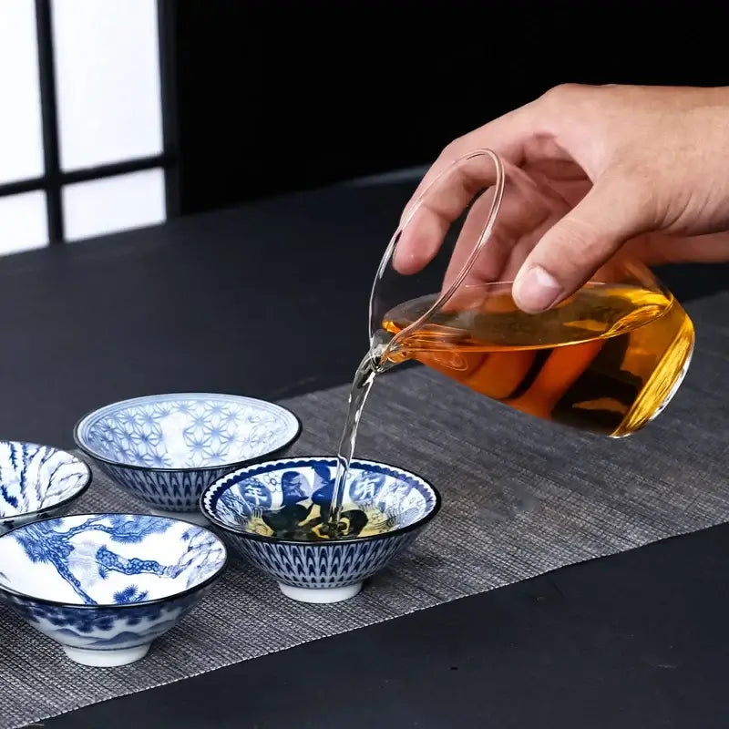 A clear glass teapot pouring amber kung fu tea into blue and white ceramic kung tea cups porcelain set