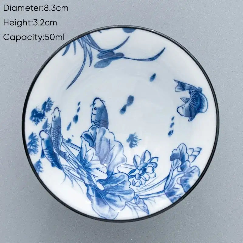 A white ceramic kung fu tea cup with a black rim and blue hand-painted fish and lotus designs for dining room use