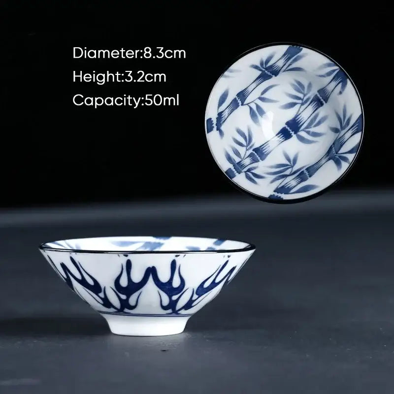 A delicate white ceramic kung fu tea cup with intricate blue bamboo and flame motifs and a glossy finish
