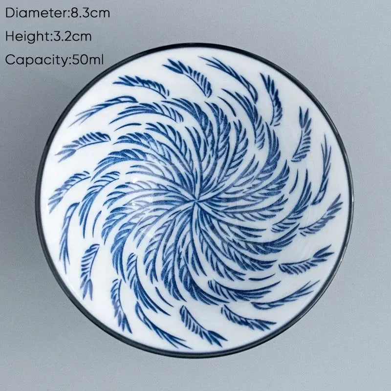 A white ceramic kung fu tea cup with a black rim and intricate blue swirling leaf pattern for dining room use