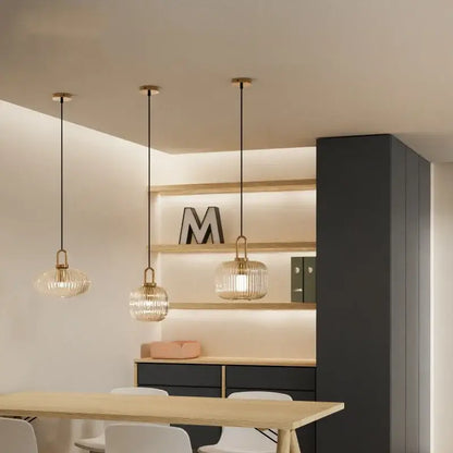 Three elegant pendant lights with brass accents and clear ribbed glass shades help create a stylish kitchen ambiance