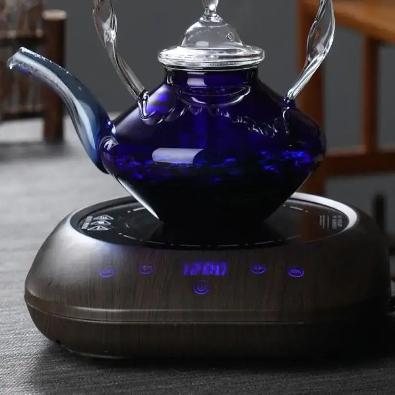 Deep blue glass teapot with twisted handles and clear lid on wooden electric heating base for kitchen decorbites blue glass