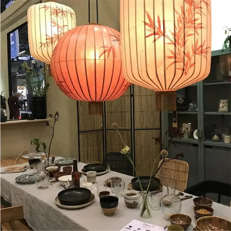 Three hanging japanese lantern painting peach fabric chandelier lights with bamboo leaf patterns in warm orange and cream tones