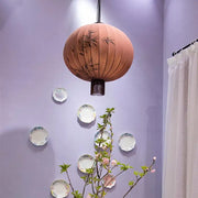A peach-colored fabric japanese lantern painting with black bamboo leaf designs and dark fringe for dining room light