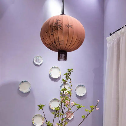 A peach-colored fabric japanese lantern painting with black bamboo leaf designs and dark fringe for dining room light